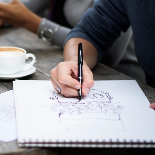 a person sitting with a coffee sketching at a table